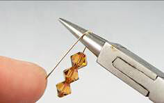 Bicone beads on a head pin being bent with pliers